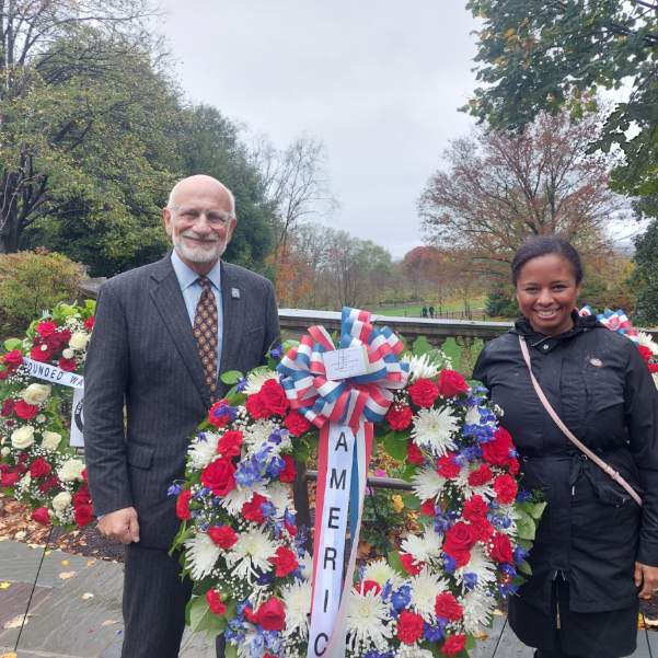 Two people standing on opposite sides of a funeral wreath